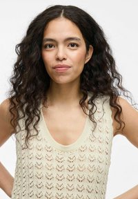 Top sin mangas de punto en color crema con un patrón texturizado y calado. Presenta un escote amplio en forma de barco y un sutil ribete acanalado en el cuello y las sisas.
