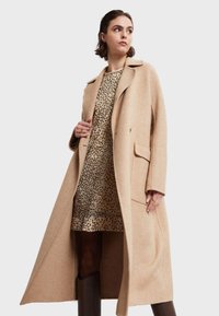 Abrigo de mezcla de lana beige con un corte largo y relajado, solapas con muesca y bolsillos laterales, combinado con un vestido de estampado de leopardo. Textura suave.