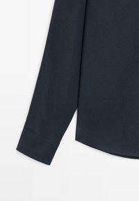 Ciemnoniebieska, długosleeve koszula o gładkiej teksturze, z zaokrąglonym dołem i zapinanym mankietem. Prosty design, bez wzorów czy akcentów.