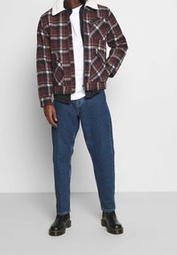 Giacca a quadri con colletto in faux shearling crema e zip frontale, abbinata a jeans blu a gamba affusolata e stivaletti neri.