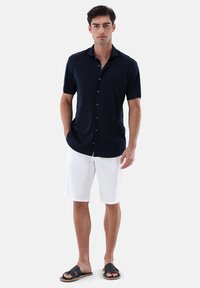 Marineblaues Hemd mit kurzen Ärmeln und Knöpfen, weiße Shorts und schwarze Sandalen. Glatter Stoff, lockere Passform und klassisches Kragen-Design.