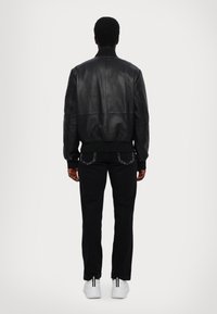 Giubbotto bomber in pelle nera con colletto e polsini a coste, abbinato a jeans neri e sneakers bianche con strisce nere sul retro.