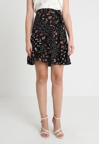 Svart omlottskjol med blommönster och vita prickar, prydd med en volangkant och knytning i midjan.