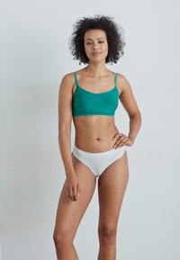 Teal bralette med tynne stropper, kombinert med hvite lav-rise bikiniunderdeler. Glatt stoff, minimalistisk design og tettsittende fasong.