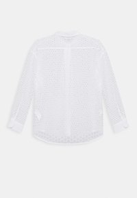 Chemise blanche à manches longues avec perforations en œillet, col boutonné et poignets. Tissu doux avec une texture légèrement transparente.