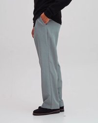 Pantalons tailleur gris clair avec une texture lisse, poches avant et coupe droite. Associés à des chaussures noires et un pull sombre.