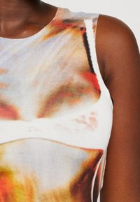 Zbliżenie na bezrękawnik z kolorowym abstrakcyjnym nadrukiem w pomarańczowym, białym i czarnym kolorze na ciemnej skórze.