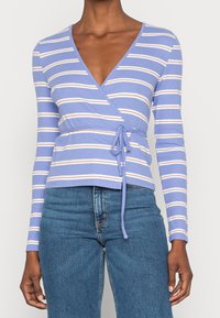 Ljusblå omlottblus med långa ärmar och v-ringning, prydd med horisontella vita och orangea ränder, med cinchade midjeband.