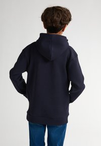 Felpa blu marina con cappuccio regolabile, tessuto morbido e polsini a coste. Disegnata con una vestibilità comoda e dettagli di cucitura a vista.