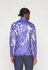 Langärmliges Sportoberteil in Lila mit abstrakten weißen und schwarzen Mustern. Hergestellt aus glattem, dehnbarem Material mit einem hohen Kragen.