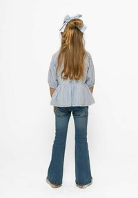 Hele halli ja valge triibuline peplum-sümmeetriline topp lühikeste puffvarrukatega, koos flared denimsse ja sobiva nööbiga pikades juustes.