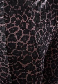 Textiel met luipaardprint, met zwarte vlekken op een vervaagde mauve achtergrond. Zachte textuur met een lichte glans, die de detail van het patroon benadrukt.