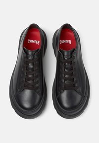 Sneaker Camper nere con solette rosse. Le scarpe presentano punte rotonde e lacci, mostrate da una prospettiva dall'alto su uno sfondo bianco.
