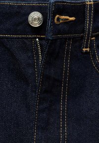 Jean en denim bleu foncé avec bouton métal visible, fermeture éclair partiellement ouverte et coutures orange sur la taille et les passants de ceinture.