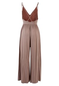 Combinaison sans manches à jambes larges avec bretelles croisées et corsage marron en V sur pantalon fluide rose poudré.
