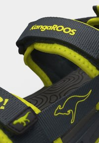 Κοντινό πλάνο λουριού σανδαλιού KangaROOS σε μαύρο και νέον κίτρινο με λογότυπο καγκουρό και επένδυση με επένδυση μαξιλαριού.