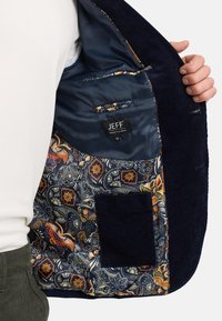 L'intérieur de la veste en velours côtelé marine présente une doublure colorée en paisley floral avec une poche et une étiquette indiquant "JEFF URBAN TAILORING."