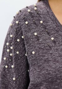 Maglione viola con una texture morbida, caratterizzato da decorazioni con perle e perline nere sulle spalle per un effetto decorativo.