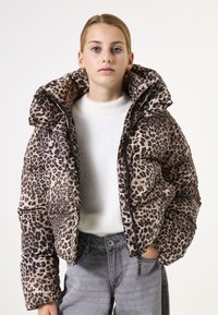Veste matelassée en imprimé léopard avec un col montant, fermeture éclair et texture matelassée. Associée à un pull blanc et un jean gris.
