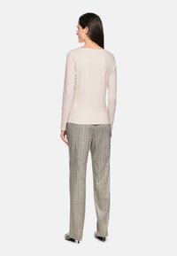 Hellbeige langärmliges Oberteil, kombiniert mit grau gestreiften Hosen. Das Outfit zeichnet sich durch eine lockere Passform und eine glatte Stofftextur aus, mit dezenten Designdetails.