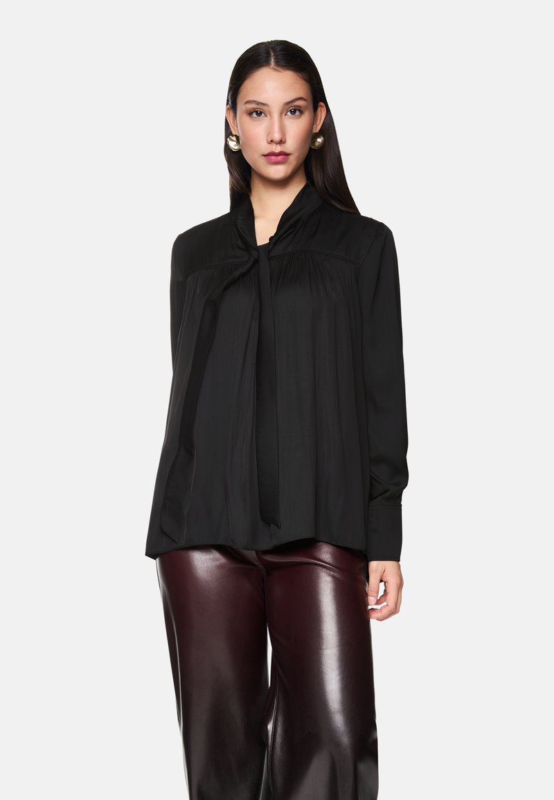 Schwarze Bluse mit langen Ärmeln, Kragen und Bindebanddetail, mit Falten und einer lässigen Silhouette, kombiniert mit burgunderfarbenen glänzenden Hosen.