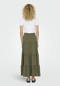 Larga falda de tiernas verdes hecha de un tejido suave; cuenta con una cinturilla elástica y un diseño fluido. Combinada con una blusa blanca sencilla.