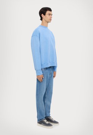 Light blue oversized sweatshirt with ribbed cuffs, paired with light blue jeans and dark sneakers. Simple design, relaxed fit.