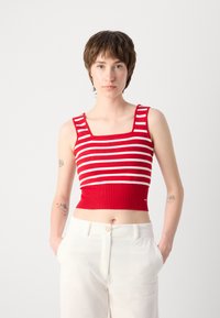 Top court à rayures rouges et blanches avec un décolleté carré et des bretelles larges, complété par un pantalon en velours côtelé de couleur claire.