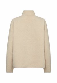 Beige színű bolyhos dzseki magas gallérral és hosszú ujjakkal. Puha tapintású és laza fazonú, látható záródás nélkül.