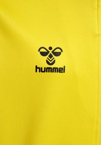 Geel stof met een gladde textuur bevat een zwart logo-ontwerp, inclusief gestileerde elementen die lijken op vleugels en een bij.