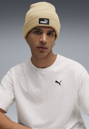 Berretto lavorato a coste beige con logo Puma nero, abbinato a una semplice maglietta in cotone bianca con un piccolo logo Puma nero sul petto.
