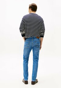 Maglione a righe blu navy e bianco a maglia con maniche lunghe, abbinato a jeans azzurri. Tasche posteriori rovinate, etichetta in pelle marrone sulla vita.