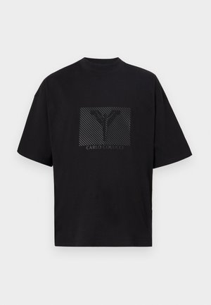 T-shirt preta de algodão com um gráfico quadrado apresentando um 'Y' em padrão e o texto "CARLO COLUCCI" em preto. Mangas curtas e corte relaxado.