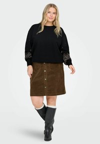 Melna džemperis ar rakstainajiem piedurkņu detaļām, brūna korduroja svārki ar priekšējiem pogām un melni augstpapēžu zābaki līdz ceļiem.