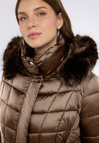 Chaqueta acolchada marrón con cuello alto y ribete de pelo sintético. Tejido liso y brillante con texturas contrastantes y detalles sutiles de costura.