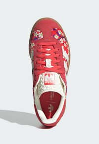 Rote Wildlederschuhe mit Blumenmuster, weißen drei Streifen, strukturiertem weißen Zungenbereich und Gummisohle. Es verfügt über flache Schnürsenkel und ein Branding auf der Zunge.