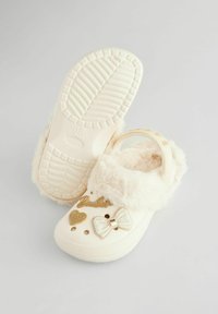 Cremefarbene Clogs mit Kunstfellfutter, goldenen Akzenten und dekorativem Schleifen. Mit Belüftungsöffnungen und strukturiertem, rutschfestem Schuhsohle.
