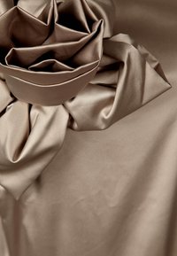 Beige satintyg med en stor, texturerad, lager-på-lager blommönster. Slät yta med subtil lyster och mjuka draperade veck.