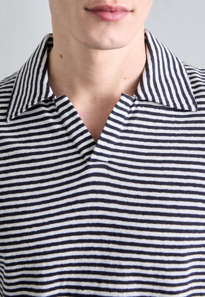 Polo rayé en bleu marine et blanc. Doté d'un col en V et d'un col classique. Fabriqué en tissu doux, affichant des rayures horizontales uniformes.