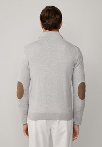 Grauer Pullover mit Kragen und langen Ärmeln, ausgestattet mit braunen Ellenbogen-Patches und einer strukturierten Oberfläche. Schlichtes und figurbetontes Design.