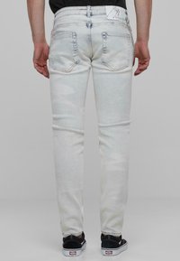 Világoskék mosott farmernadrág, slim fit, öt zsebbel, diszkrét kopással, varrott varratokkal és márkázott címkével a deréknál.