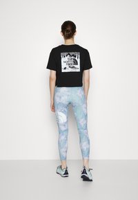 Svart kortärmad t-shirt med vitt grafikdesign; ljusblå tights med batikmönster; träningsskor med svarta och mintgrön accent.