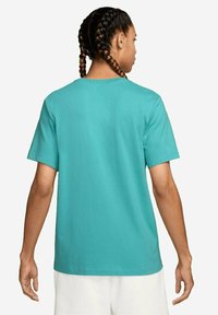 T-shirt in cotone turchese con maniche corte, scollo rotondo e vestibilità rilassata. Texture liscia, design semplice, vista posteriore mostrata.