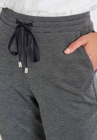 Pantalons de jogging gris à motif avec une taille élastique, corde de serrage et poches latérales, présentant une finition en tissu texturé.