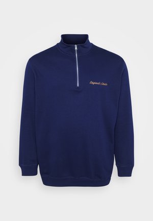 Felpa mezza zip blu navy realizzata in tessuto morbido. Presenta un colletto alto, polsini a costine e la scritta "Originals Studio" ricamata in un colore a contrasto.