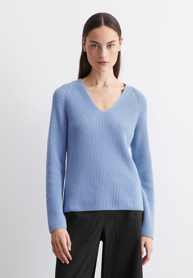 Helles blaues, geripptes Strickpullover mit V-Ausschnitt und langen Ärmeln; weiche Textur und figurbetontes Design. Kombiniert mit schwarzen, taillierten Hosen.