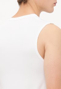 White sleeveless tank top with a round neckline. Smooth cotton fabric with a fitted design. Visible stitching along the armholes and neckline.