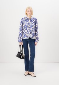 Floral patterned lightweight jacket in blue and cream, featuring a round collar and two front pockets, paired with dark blue jeans and beige flats.