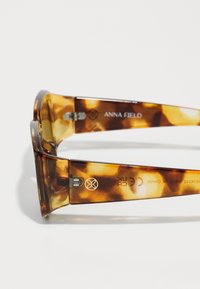 Tortoiseshell sunglasses with a thick frame, featuring a smooth finish and logo detailing on the temples. Metallic accents on the hinges.