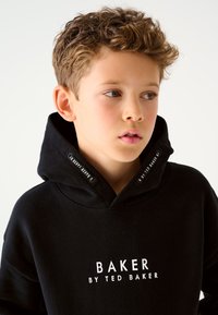 Must kapuutsiga dressipluus valge tekstiga "BAKER BY TED BAKER", millel on suur kapuuts ja brändilogoga paelad. Sile kangas.
